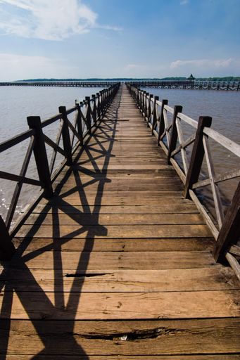 A vertical shot of an old wooden pier in front of the see with a beautiful cloudy sky in the background