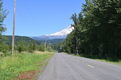 A straight road leading to a forest and mountain landscape under a clear sky