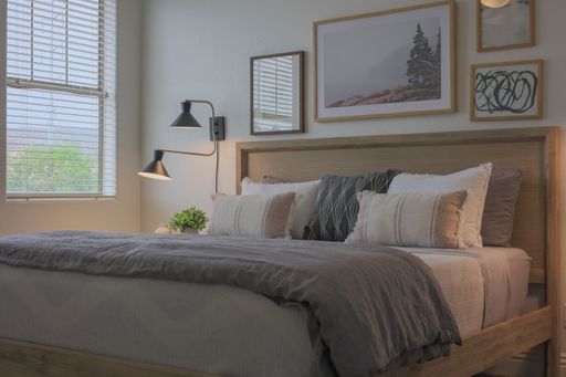 A modern decorated bedroom with a bed covered by gray and  white bedclothes and pillows with beautiful patterns and the  pictures above