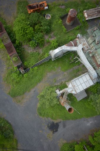 A vertical high angle shot of an abandoned factory with bright green plants growing