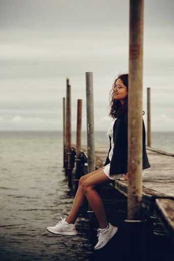 A vertical of a South Asian girl sitting on a wooden dock.