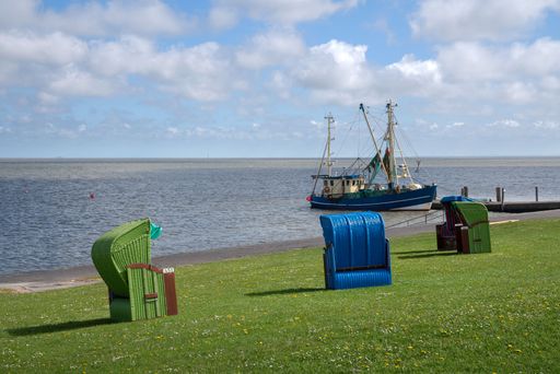 The landscape of the Pellworm shore with beach chairs and a ship moored at the pier