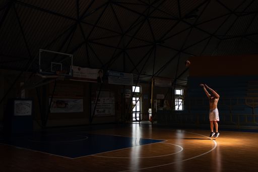 The basketball player shoots the ball while being enlightened by the sun