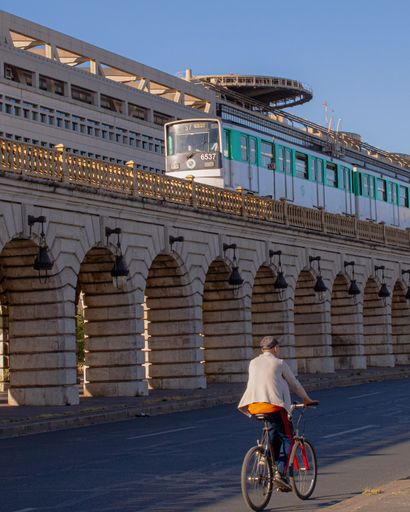 A metro in Paris passing in front of Bercy, with a cyclist on the road, in a vertical shot