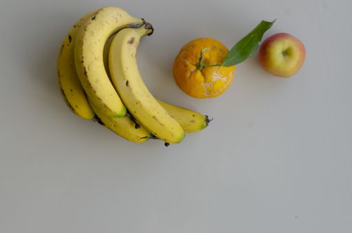 A flat lay shot of ripe bananas, an orange and an apple on a gray surface