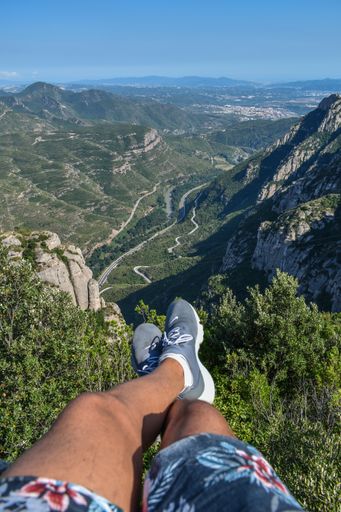 A vertical shot of a person's legs near mountains covered in lush forests