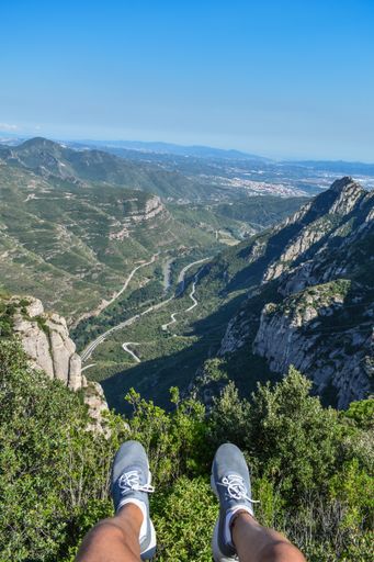 A vertical shot of a person's legs near mountains covered in lush forests