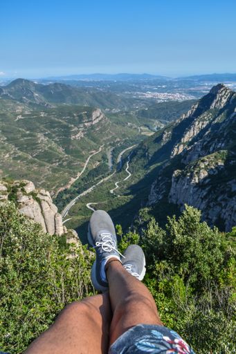 A vertical shot of a person's legs near mountains covered in lush forests