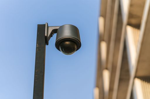 The low-angle view of a black security camera column by a residential building before the blue sky