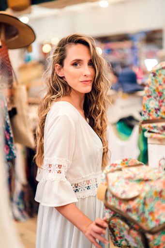 A young blonde sexy Caucasian woman in a white tunic standing in a store and looking at a camera