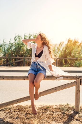 A young blonde sexy Caucasian woman wearing a white tunic and shorts sitting on the wood