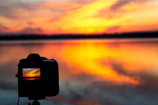 A closeup of a camera shooting the scenic sunrise with its reflection on the sea