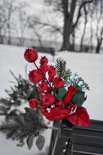 A Christmas decoration with red berries and flowers against a blurry background, vertical shot