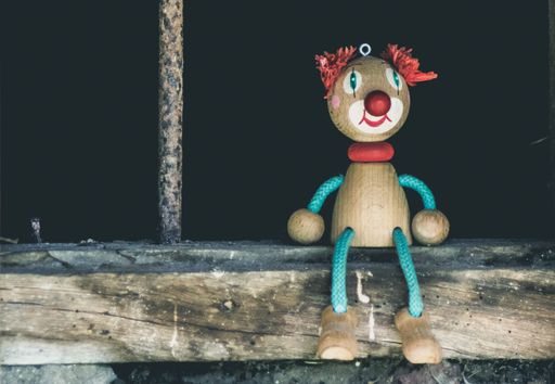 A closeup shot of a wooden figure of a smiling clown on a black background