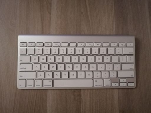 A top view of a wireless silver keyboard on a wooden surface
