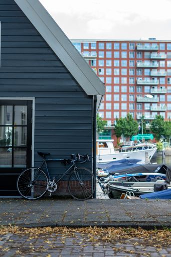 A vertical shot of a bicycle parked near a small cottage surrounded by boats in the Westerdok area, Amsterdam