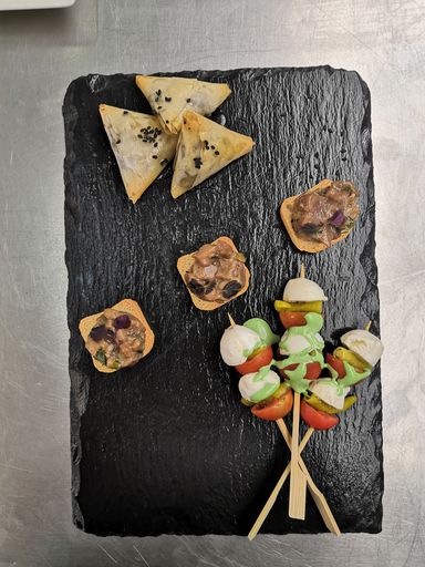 A shot of samsas, canapes and snack skewers on a black plate