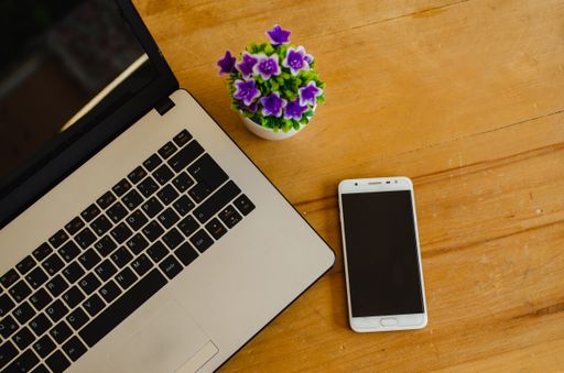 A high angle closeup shot of a laptop and a smartphone next to on a pot of flowers wooden table
