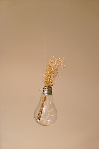 A vertical closeup shot of flower decoration in a hanging light bulb isolated on a pink background