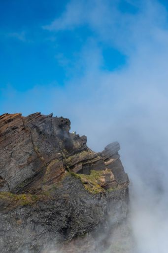 A vertical shot of a rocky mountain under the foggy sky