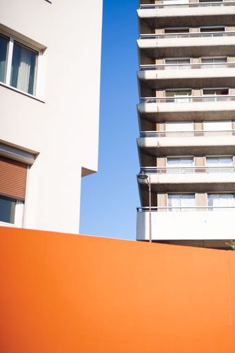 A two buildings with windows and balconies built next to each other and an orange wall under those