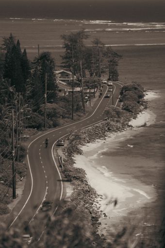 A vertical shot of a narrow road constructed near the sea in black and white