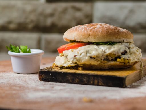 A closeup of a chicken filet burger with white sauce served on a wooden tray