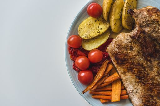 A flat lay shot of fried meat, potatoes, carrots and tomatoes on a plate