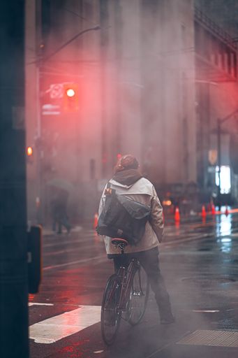 A vertical back view of a male riding a bike in the street on a rainy day in Toronto