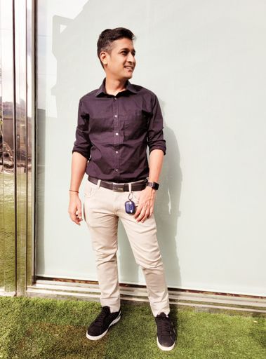 Full body of handsome Indian young man in smart casuals looking away and standing on sunny summer day