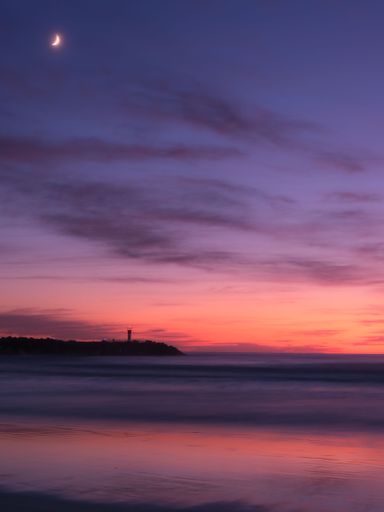 A vertical shot of a beautiful sunset over the ocean with pink clouds in the sky