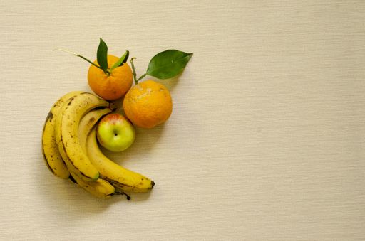 A flat lay shot of ripe bananas, oranges and an apple on a beige surface