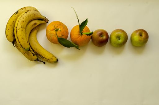 A flat lay shot of ripe bananas, oranges and apples on a beige surface
