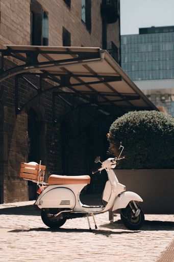 A vertical shot of white scooter parked on sidewalk near the building under sunlight