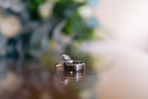 A selective focus shot of wedding bands on a shiny surface - bride's gold and diamond ring and groom's plain silver ring