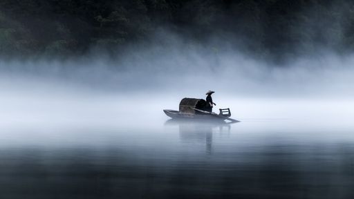 A man on a wooden hunting boat floating on the river in the fog