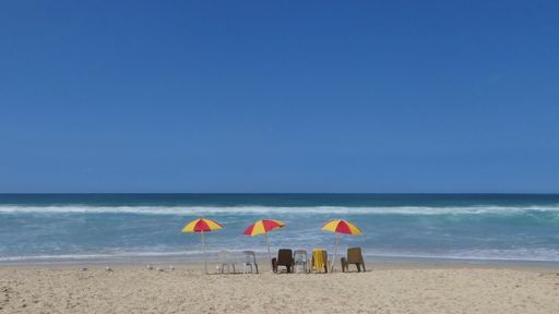 scenic view of red and yellow beach umbrellas with plastic chairs in a row on sand at the beach against clear blue sky and space for text
