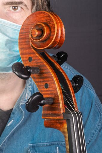A vertical shot of a musician wearing a sanitary mask holding a cello - concept of the new normal