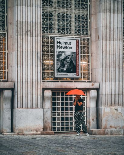 A vertical shot of a guy with umbrella waiting in the rain with vintage building in the background