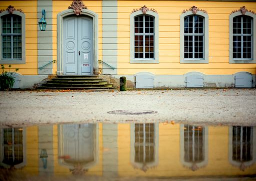 A yellow house with grey window frames and a wooden door reflected in the water surface