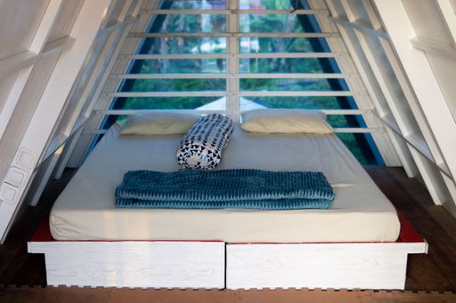 An inside of a triangle roof cottage room with a white bed and pillows on it
