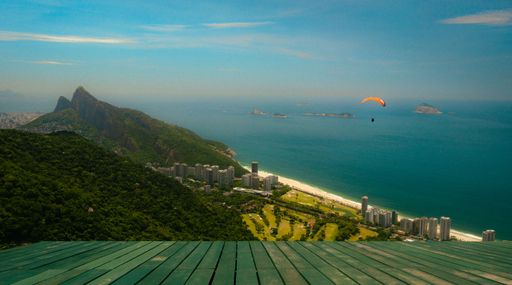 A beautiful view of a parachuter over a calm blue sea with tall green hills overlooking it