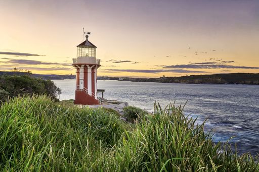 A beautiful shot of a small red and white lighthouse at the shore of the sea during sunset