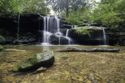 A beautiful shot of water flowing down the rocks into a pond in the forest with trees in the background