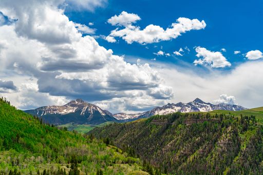 A gorgeous view of vast green mountains with snow on their peaks under a white and blue cloudy sky in Rocky Mountain National Park, Colorado