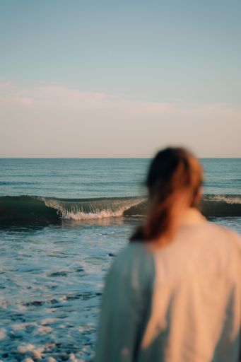 A vertical closeup of the woman looking at the ocean wave.
