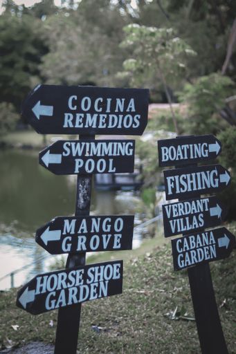 A vertical shot of black signs showing the directions of boating, swimming pool, and fishing by Bantug Lake