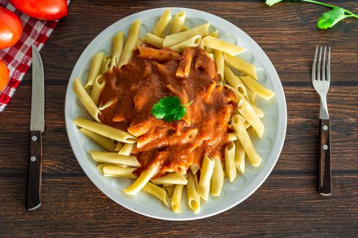 typical italian penne pasta on wooden background with tomato sauce