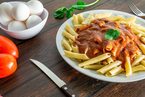 typical italian penne pasta on wooden background with tomato sauce