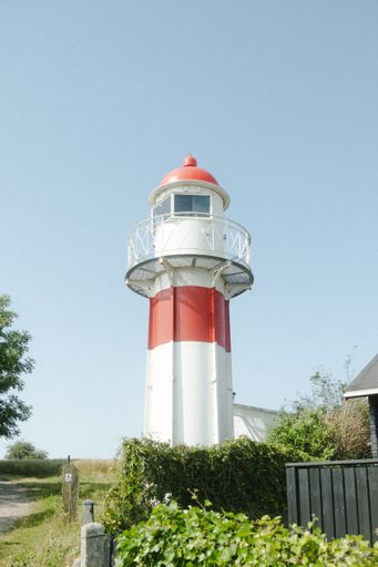 A low angle view of red and white lighthouse under blue bright sky